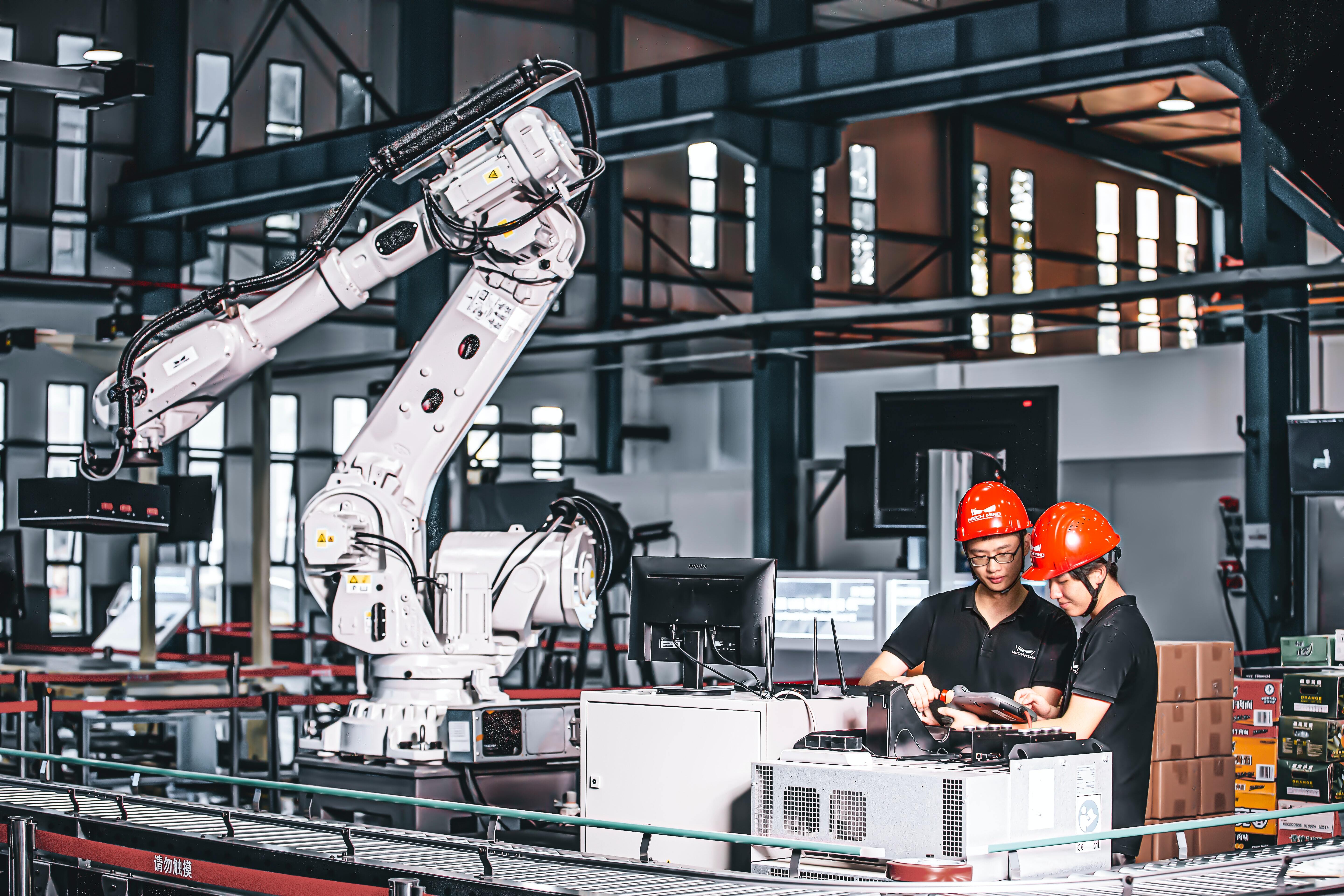 2 Arbeiter mit Helm neben Roboterarmn