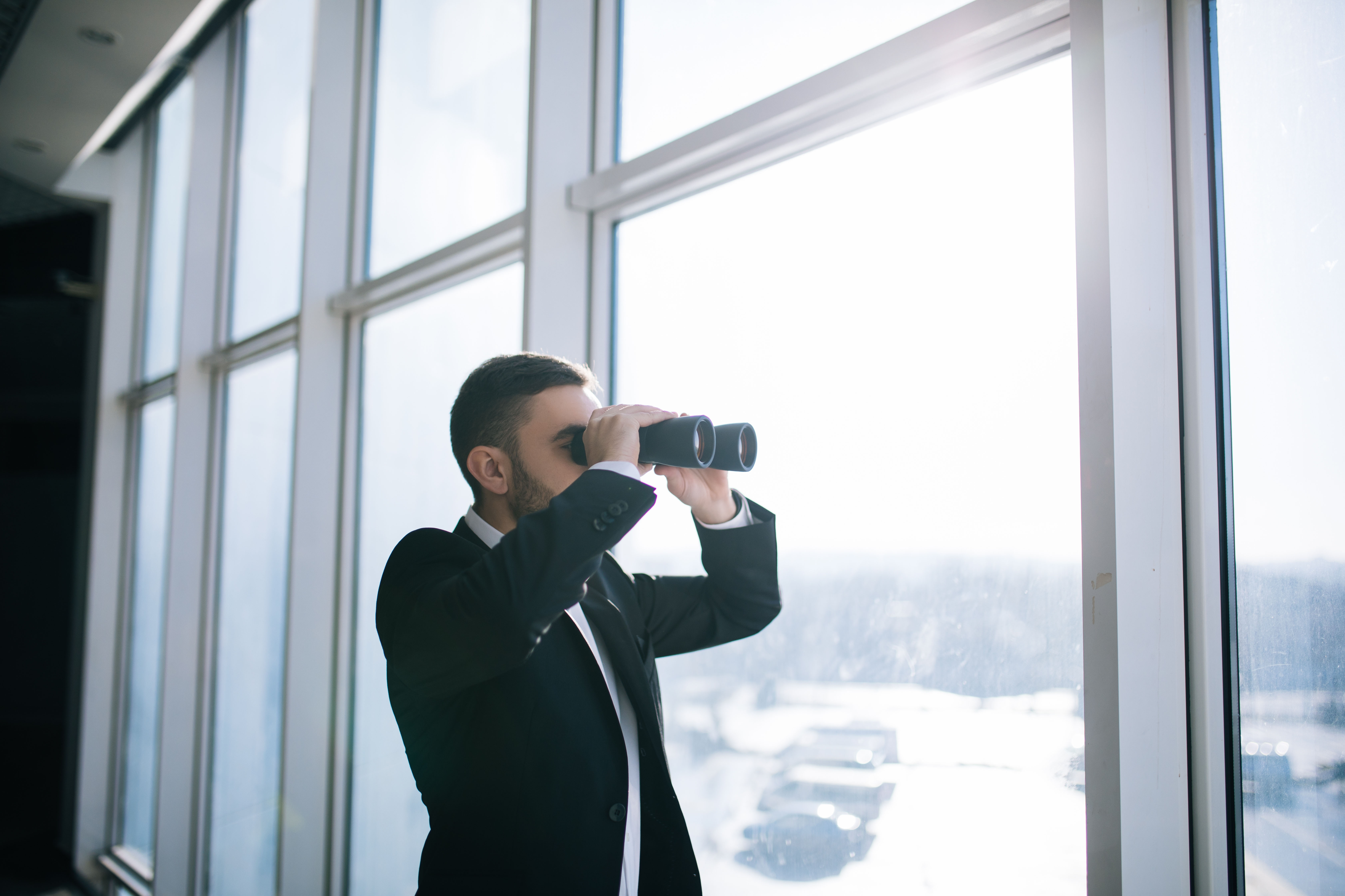 Mann schaut mit Fernglas aus Fenster