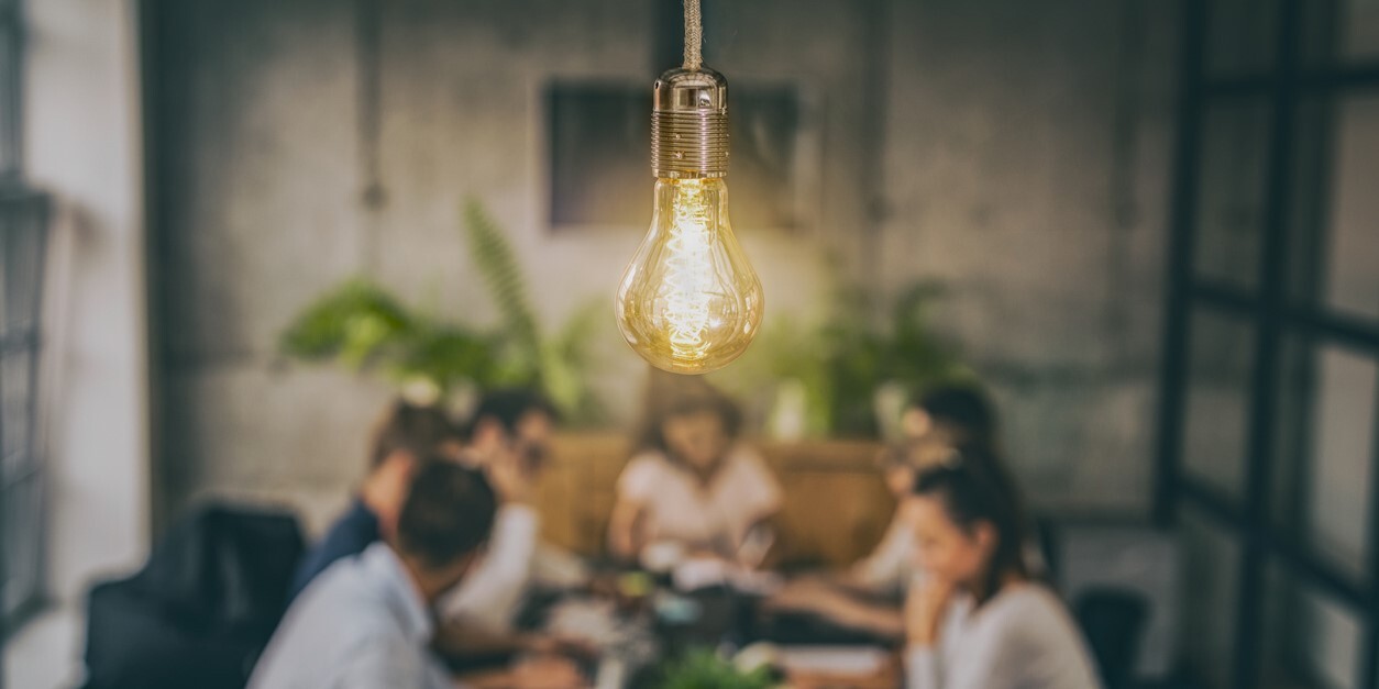 Hängende leuchtende Glühbirne. Im Hintergrund sitzen Geschäftsleute an einem Tisch und diskutieren