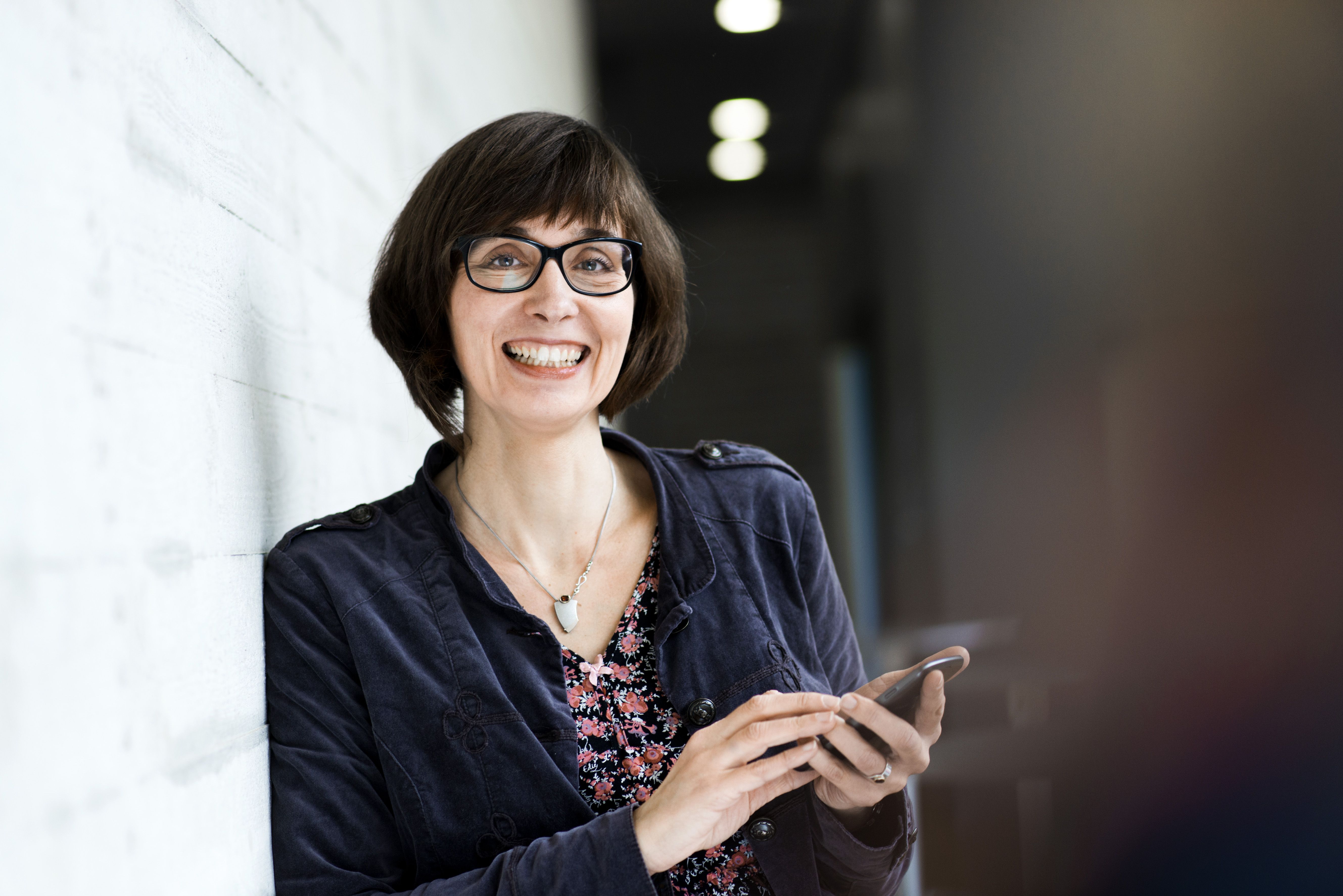 Frau mit Smartphone lehnt an Wand